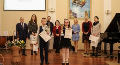 sala koncertowa szkoły muzycznej w Lublińcu na scenie stwoji dwójka dzieci zwycięsców Grand Prix Festiwalu dla Pianistów. Dzieci trzymają w rękach dyplomy i puchary, za nimi stoją członkowie komisjii konkursowej oraz wiceburmistrz Anna Jonczyk-Drzymała Lublińca wraz z przedstawicielem Rady Powiaty Panią Naczyńską