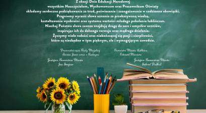 Życzenia dla nauczycieli na pisane białą kredą na zielonej tablicy za biurkiem, na którym leżą książki oraz bukiet kwiatów