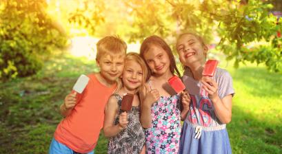 grupa dzieci jedzących lody w ogrodzie, miedzy drzewami 