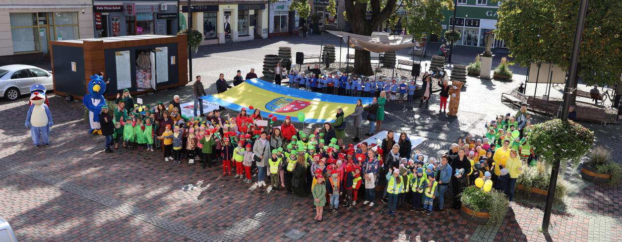 na rynek miejski przyszły najstarsze grupy Lublinieckisz przedszkolaków, za grupkami dzieci ustawionych w grupkach stoją władze lublińca z rozciągnietą flagą lublińca