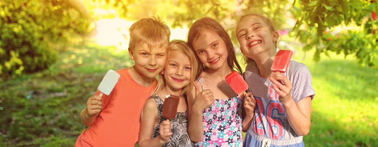 grupa dzieci jedzących lody w ogrodzie, miedzy drzewami 